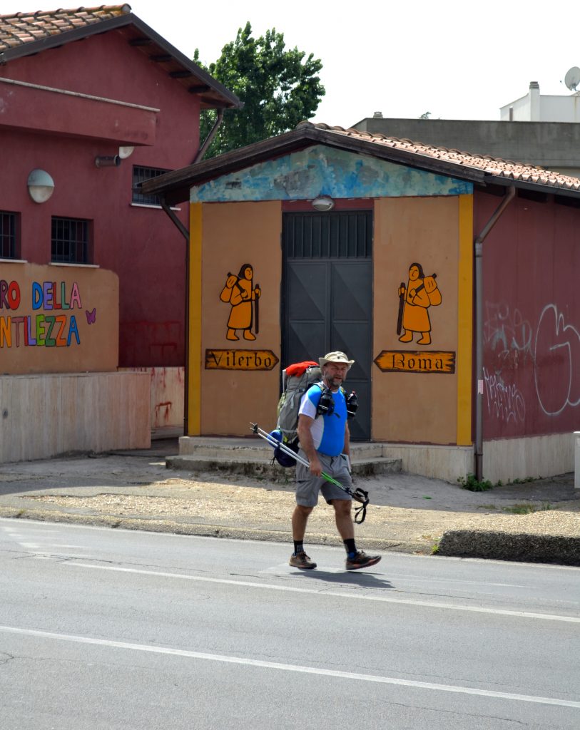 Il primo camminatore che passa davanti al murales con le indicazioni Roma e Viterbo della Via Francigena